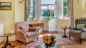 A room with a striped armchair, a tufted armchair, a wooden coffee table, a vase of yellow flowers, and a painting on the wall. - 3 Bed in Brecon (oc-bn134) (Brecon)