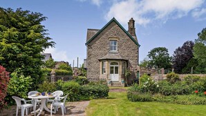 A stone house with a central door, a small porch, and a garden with a lawn and potted plants. - 3 Bed in Brecon (oc-bn134) (Brecon)