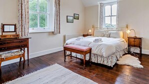 A bedroom with a large bed, two bedside tables, a wooden dresser, a bench, and two windows with curtains. - 3 Bed in Brecon (oc-bn134) (Brecon)