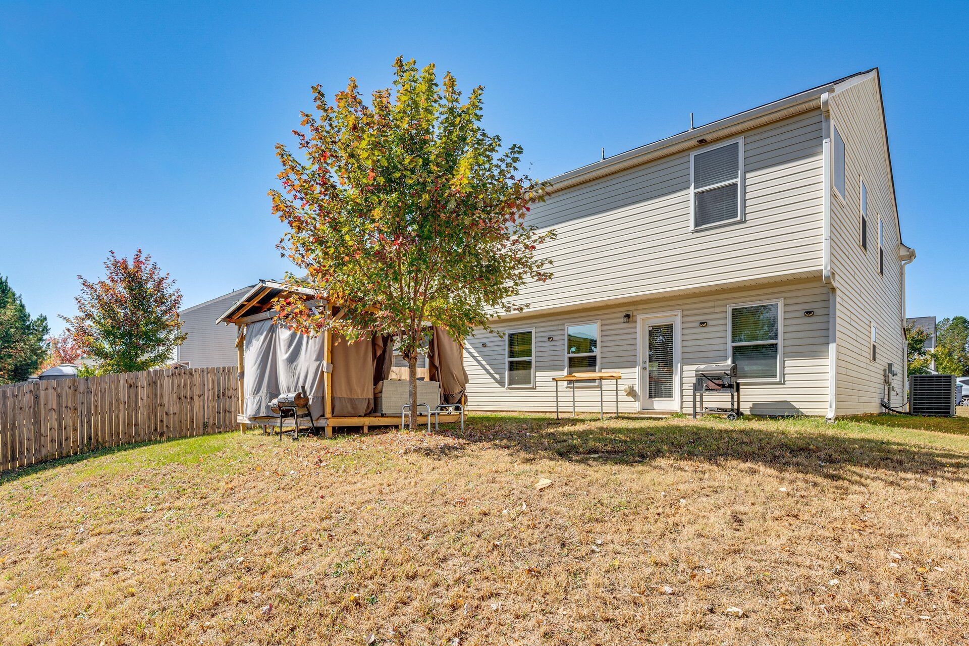 A two-story house with a covered outdoor seating area and a tree in front.