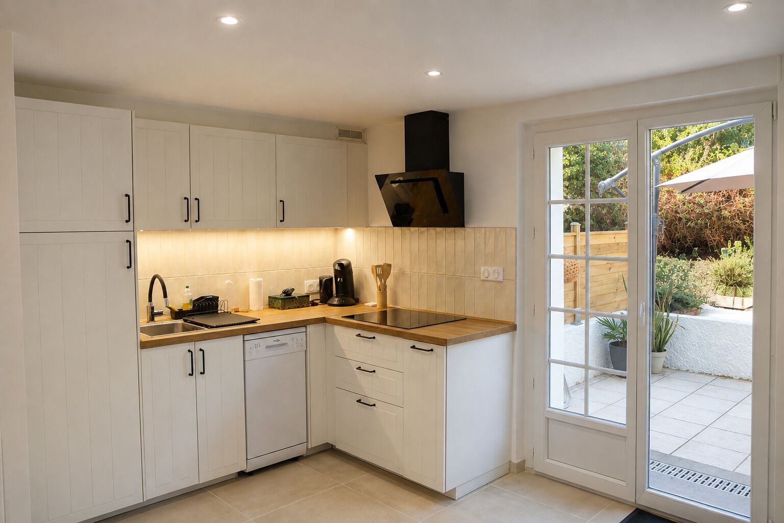 A modern kitchen with white cabinets, a black range hood, and a window to the outside.