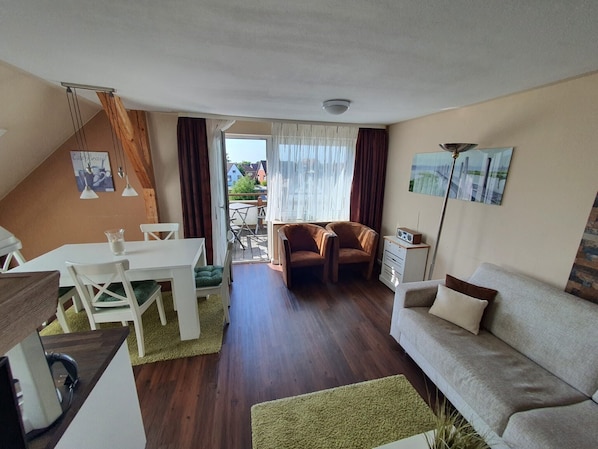 A living room with a sofa, chairs, a dining table, and a view through a glass door to the outside. - North Sea Vacation in a Prime Location—Centrally Located and Close to the Beach in Büsum, Apartment 6 (Büsum)