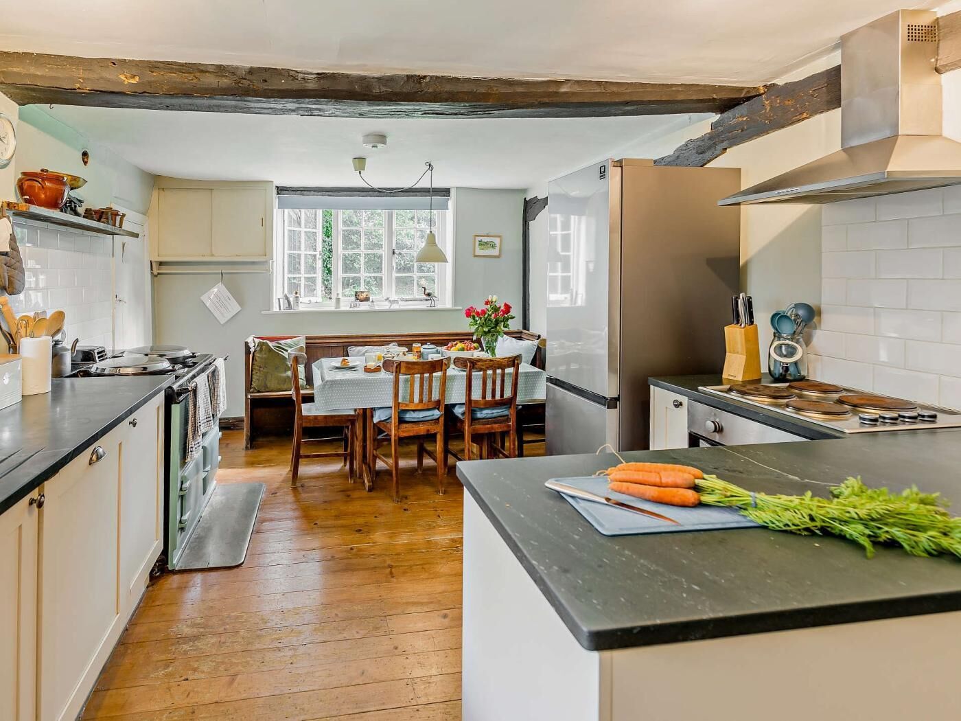 A kitchen with wooden floors, a dining table with chairs, a refrigerator, and a countertop with vegetables.