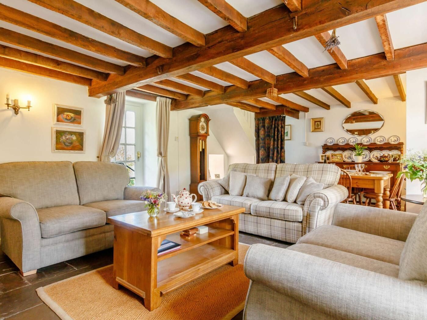 Un salon chaleureux avec un plafond en bois, un ensemble de canapés, une table basse et une table à manger avec des chaises.