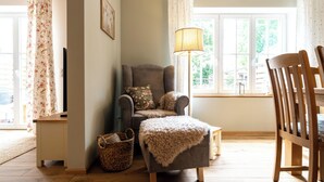 Ein gemütliches Wohnzimmer mit einem grauen Sessel, einem Holzstuhl, einer Stehlampe und einem Fenster mit Vorhängen.