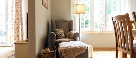 A cozy living room with a grey armchair, a wooden chair, a floor lamp, and a window with curtains.