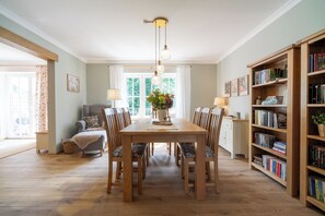 Ein Essbereich mit einem Holztisch und Stühlen, einem Bücherregal und einem Fenster mit Vorhängen.
