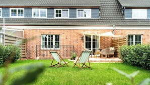 Ein Ziegelhaus mit Terrasse, zwei Liegestühle und einem Tisch.