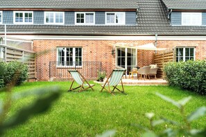 Ein Ziegelhaus mit Terrasse, zwei Liegestühle und einem Tisch.