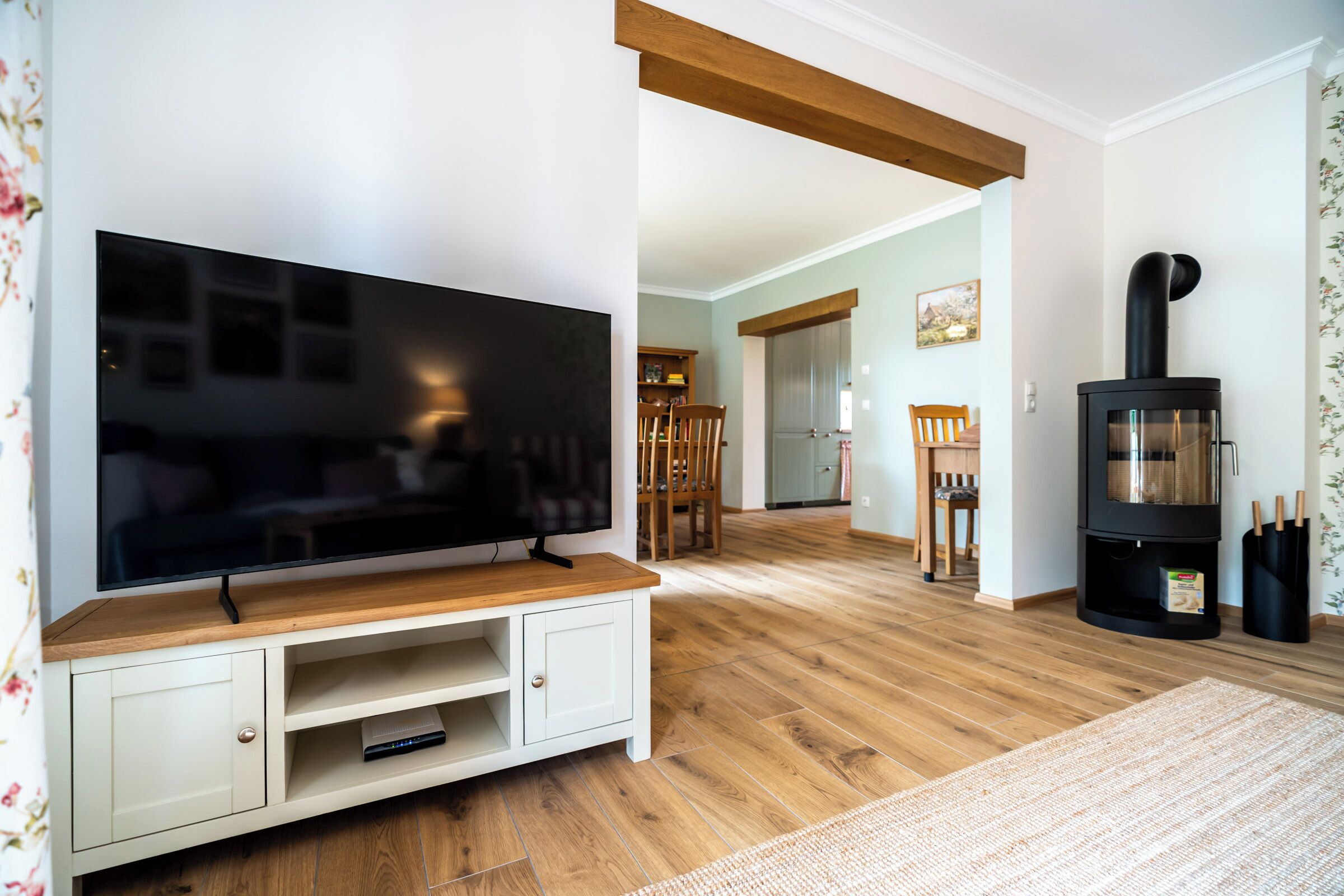 A living room with a flat-screen TV on a wooden stand, a fireplace, and a dining area with chairs and a table.