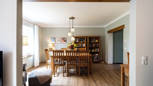 Ein Essbereich mit einem Holztisch und Stühlen, einer Hängeleuchte und einem Bücherregal im Hintergrund.