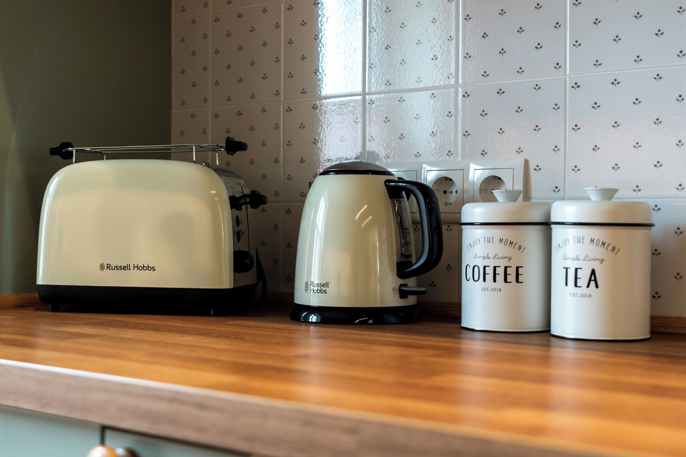 A kitchen counter with a toaster, a kettle, and two containers labeled 'COFFEE' and 'TEA'.