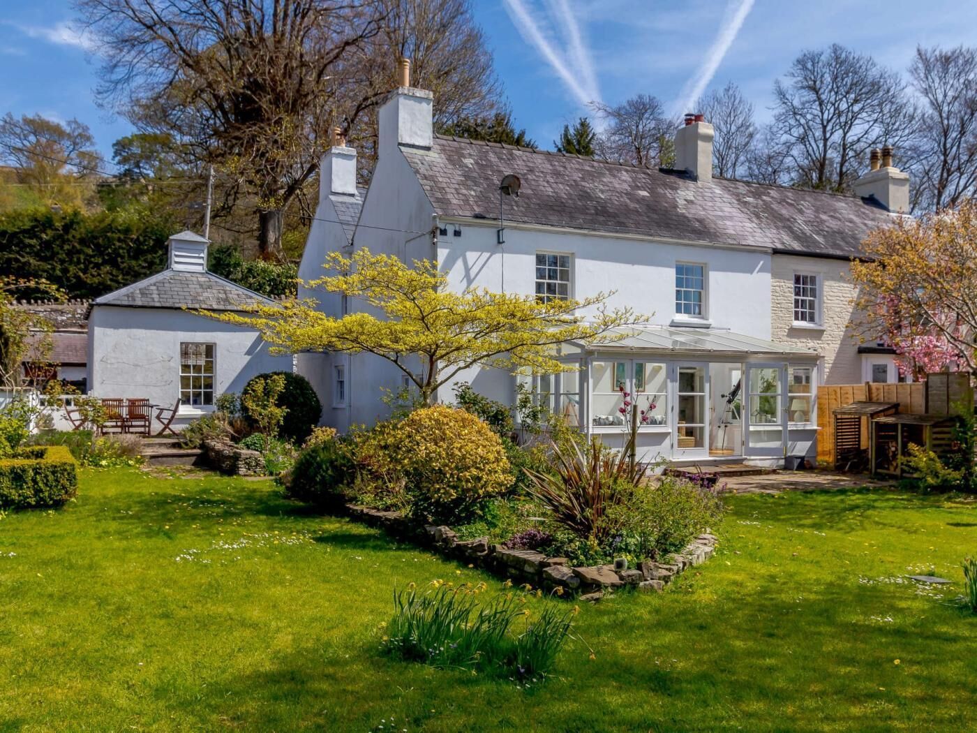 A traditional white house with a conservatory, surrounded by a well-maintained garden.