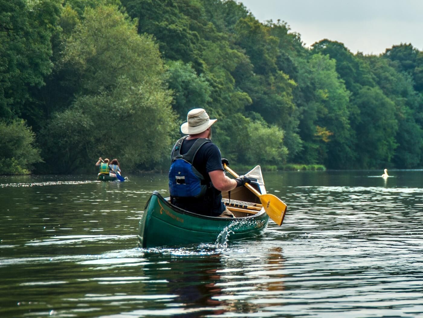 Une personne dans un canoë, sur une étendue d’eau calme, entourée d’une végétation luxuriante.