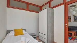 Ein Schlafzimmer mit einem Bett, einem Kleiderschrank, einem kleinen Tisch und einer Tür zu einem Wohnbereich.