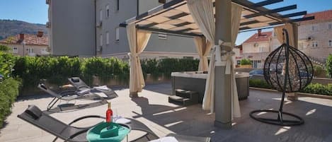 Un espacio al aire libre con sillones reclinables, una mesa y una pérgola con cortinas.