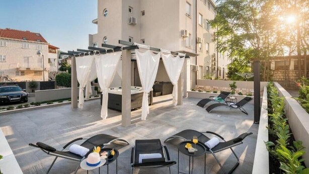 Eine Dachterrasse mit Außenbestuhlung, einer Pergola mit weißen Vorhängen und Blick auf die umliegenden Gebäude.