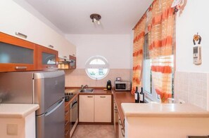 Eine kleine Küche mit Kühlschrank, Backofen, Mikrowelle und einem Fenster mit Vorhängen.