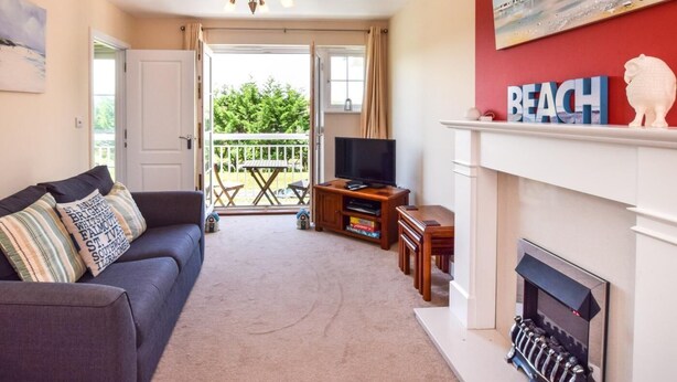 Ein Wohnzimmer mit Sofa, Fernseher, Kamin und einem Balkon mit Gartenmöbeln.