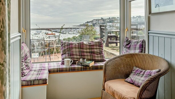 A room with a large window, wicker furniture, and a view of a marina. - 2 Bed in Brixham (oc-bx019) (Brixham)