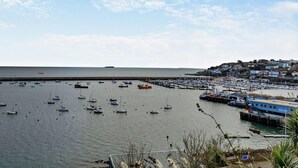 A coastal marina with numerous boats docked, a pier extending into the water, and a hillside settlement in the background. - 2 Bed in Brixham (oc-bx019) (Brixham)