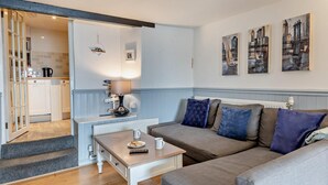 A living room with a sofa, coffee table, and a kitchen area visible through an open door. - 2 Bed in Brixham (oc-bx019) (Brixham)