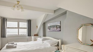 A bedroom with a bed, a bedside table, a dresser, a window with curtains, a ceiling fan, and a painting on the wall. - 2 Bed in Brixham (oc-bx019) (Brixham)