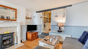 A living room with a fireplace, television, sofa, and a small table with a lamp. - 2 Bed in Brixham (oc-bx019) (Brixham)