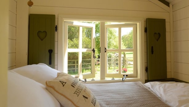 Ein Schlafzimmer mit einem Bett, einem Fenster mit Blick auf Grünflächen und herzförmigen Verzierungen an den Wänden.