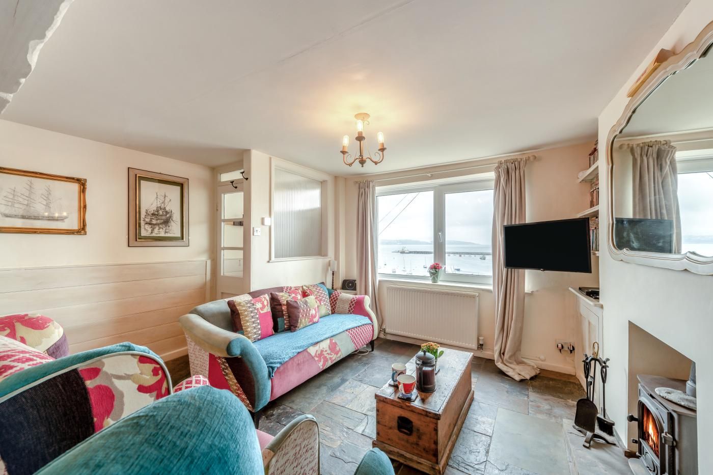 A cozy living room with a sofa, armchairs, a fireplace, a television, and a view of the sea.