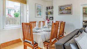 Uma área de refeições com mesa posta para quatro pessoas, cadeiras de madeira, uma estante de livros e um quadro na parede.