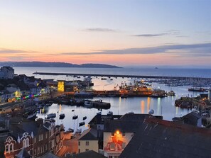 Ein Hafen im Abenddämmerung mit Booten, einer Brücke und Gebäuden entlang des Ufers.