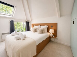 Een slaapkamer met een groot bed, een nachtkastje met een lamp en een raam met gordijnen.