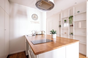 Eine moderne Küche mit Holzauszug, weißen Schränken, einem eingebauten Backofen und einer Wanduhr.