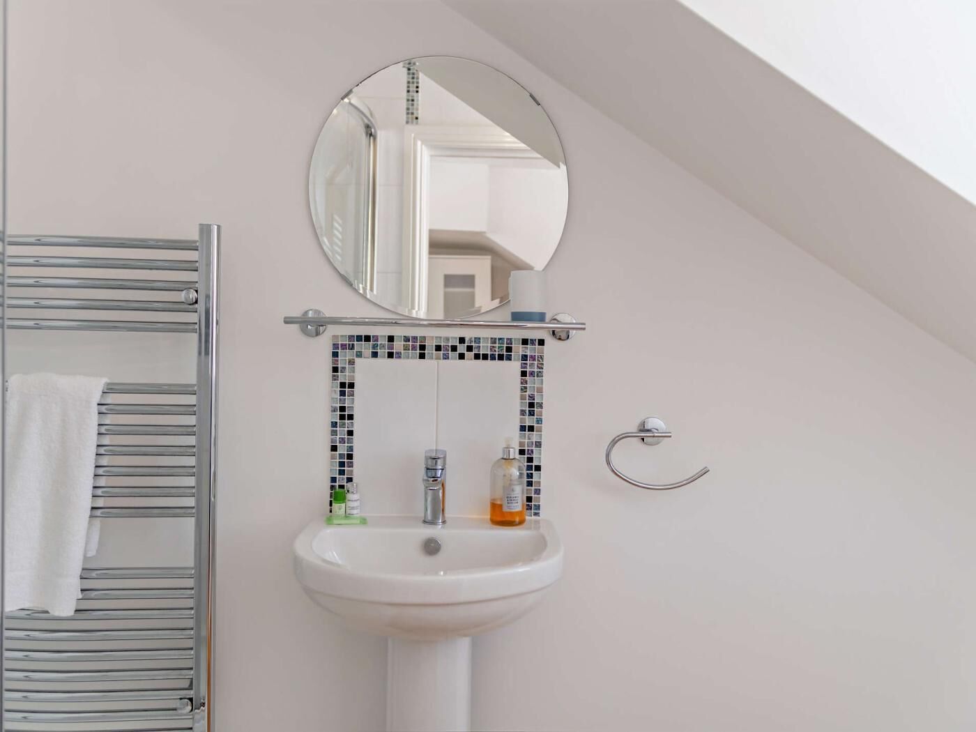 Une salle de bain avec un lavabo blanc, un miroir, un porte-serviettes et un mur recouvert de carreaux.