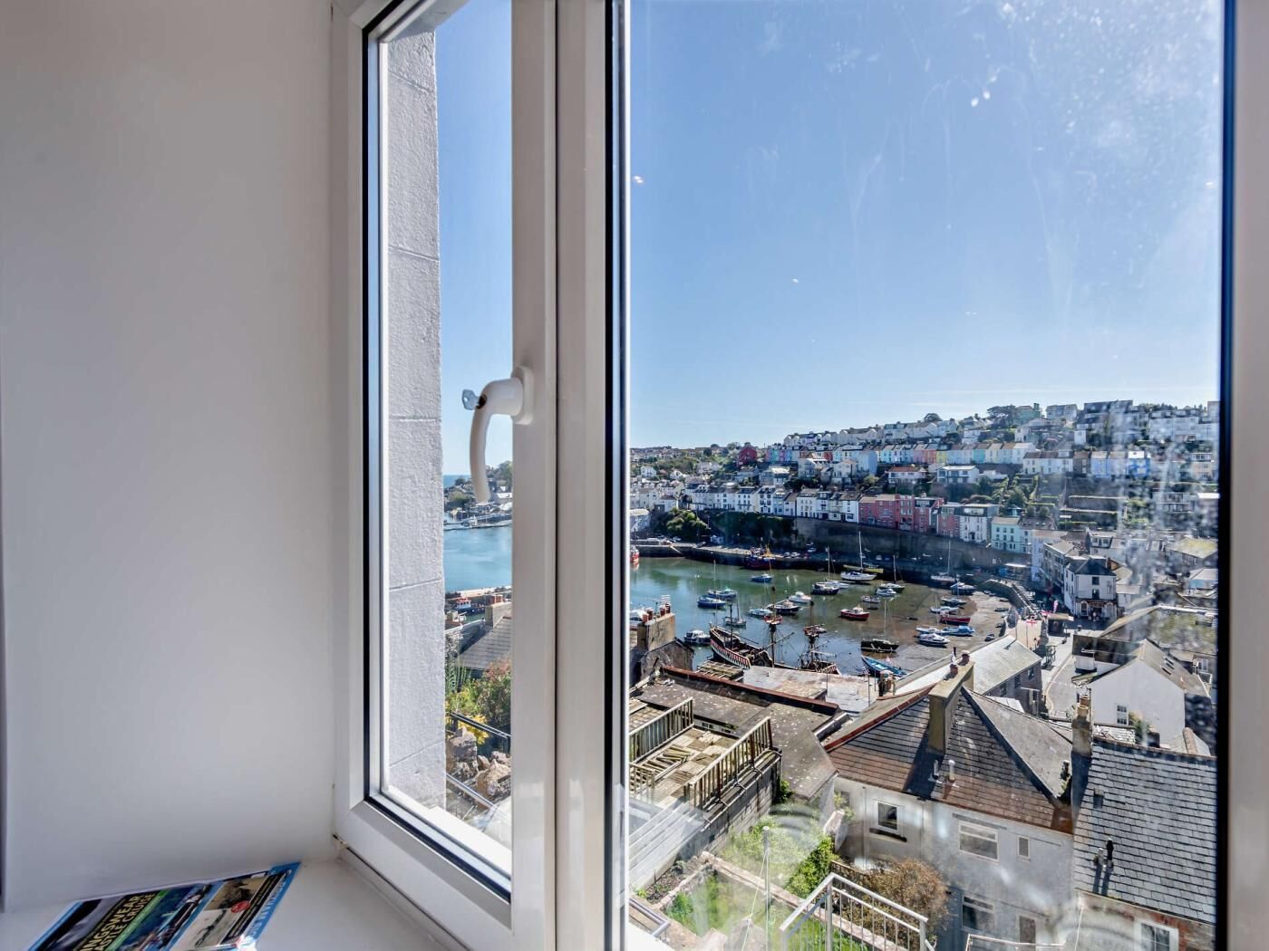 A view through a window of a coastal town with buildings, a harbor, and boats.
