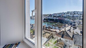 Une vue à travers une fenêtre sur une ville côtière, avec ses bâtiments, son port et ses bateaux.