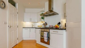 A modern kitchen with white cabinets, a stainless steel range hood, and a wooden floor. - 2 Bed in Ilfracombe (oc-caps8) (Ilfracombe)