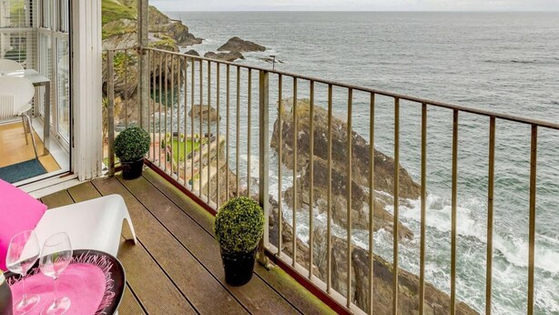 A balcony with a view of the sea, a dining area with chairs and a table, and two potted plants. - 2 Bed in Ilfracombe (oc-caps8) (Ilfracombe)
