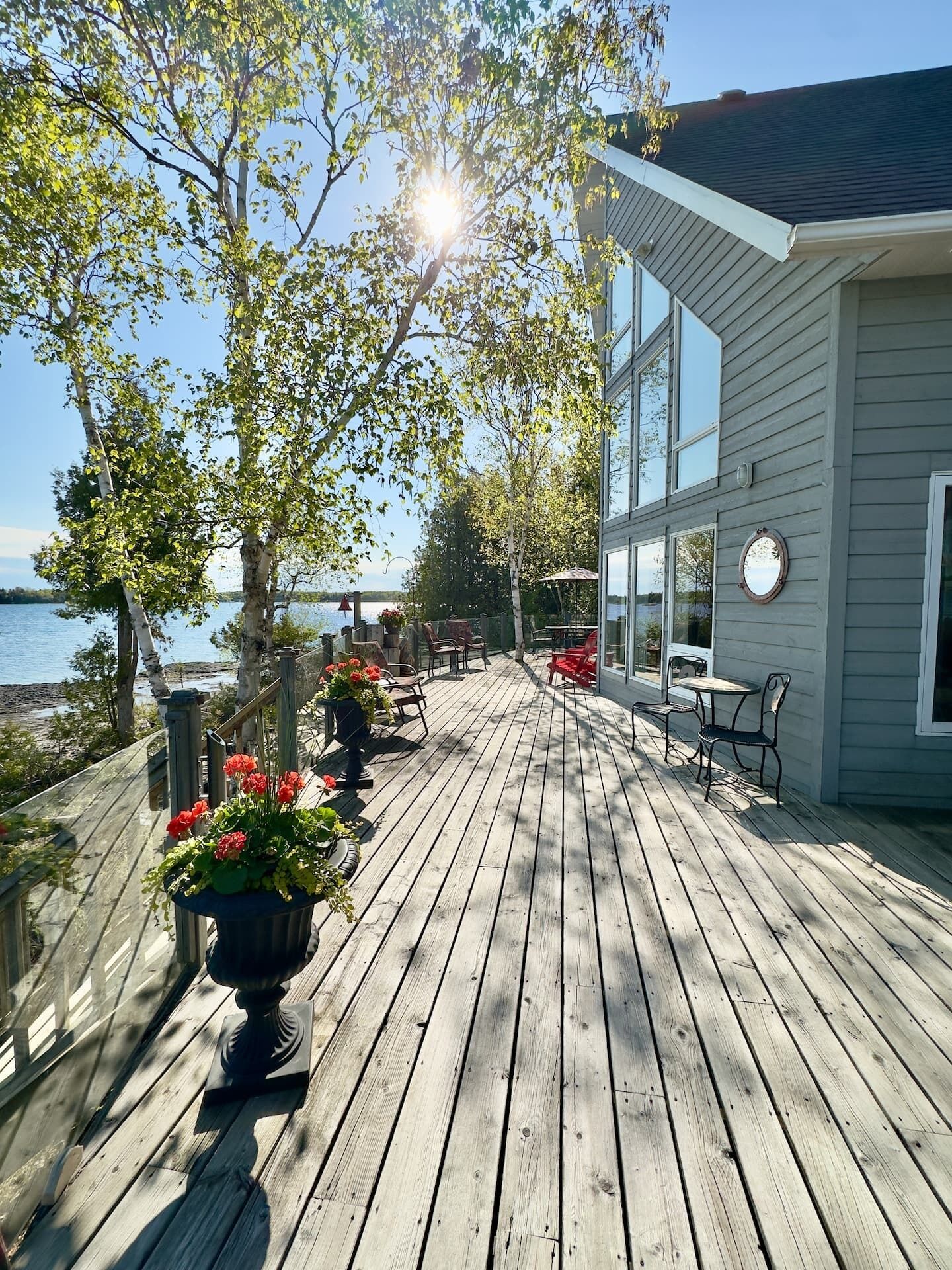 Une terrasse en bois avec des sièges extérieurs, donnant sur une étendue d’eau, et un bâtiment doté de grandes fenêtres.