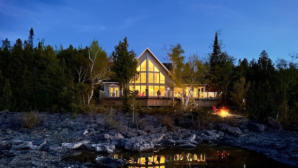 Un lodge con un edificio principale ampio e una struttura più piccola, circondato da alberi e da una riva rocciosa.