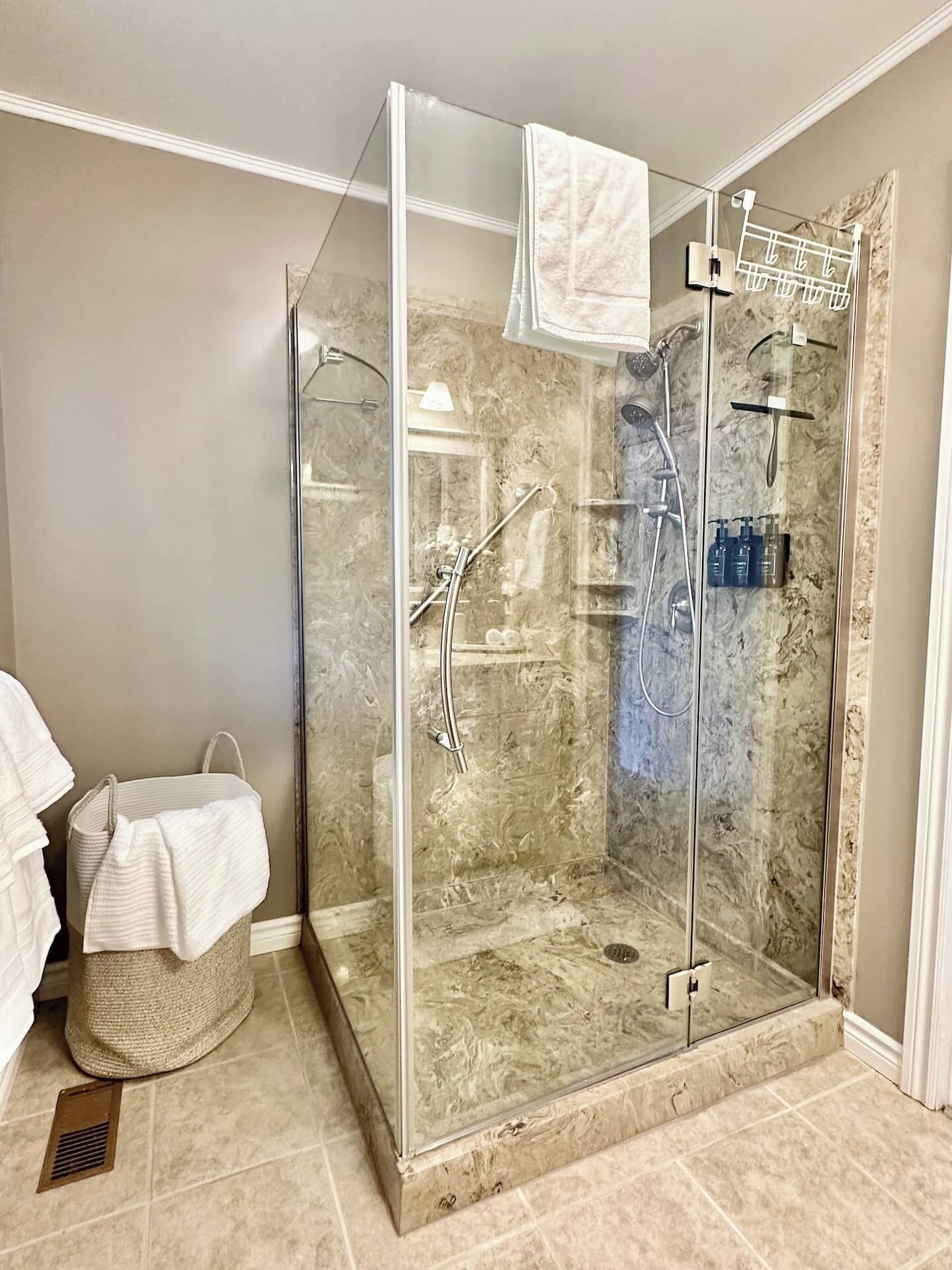 Eine begehbare Dusche mit Glaswänden, einer Marmorwand, einem Handtuchhalter und einem kleinen Korb.