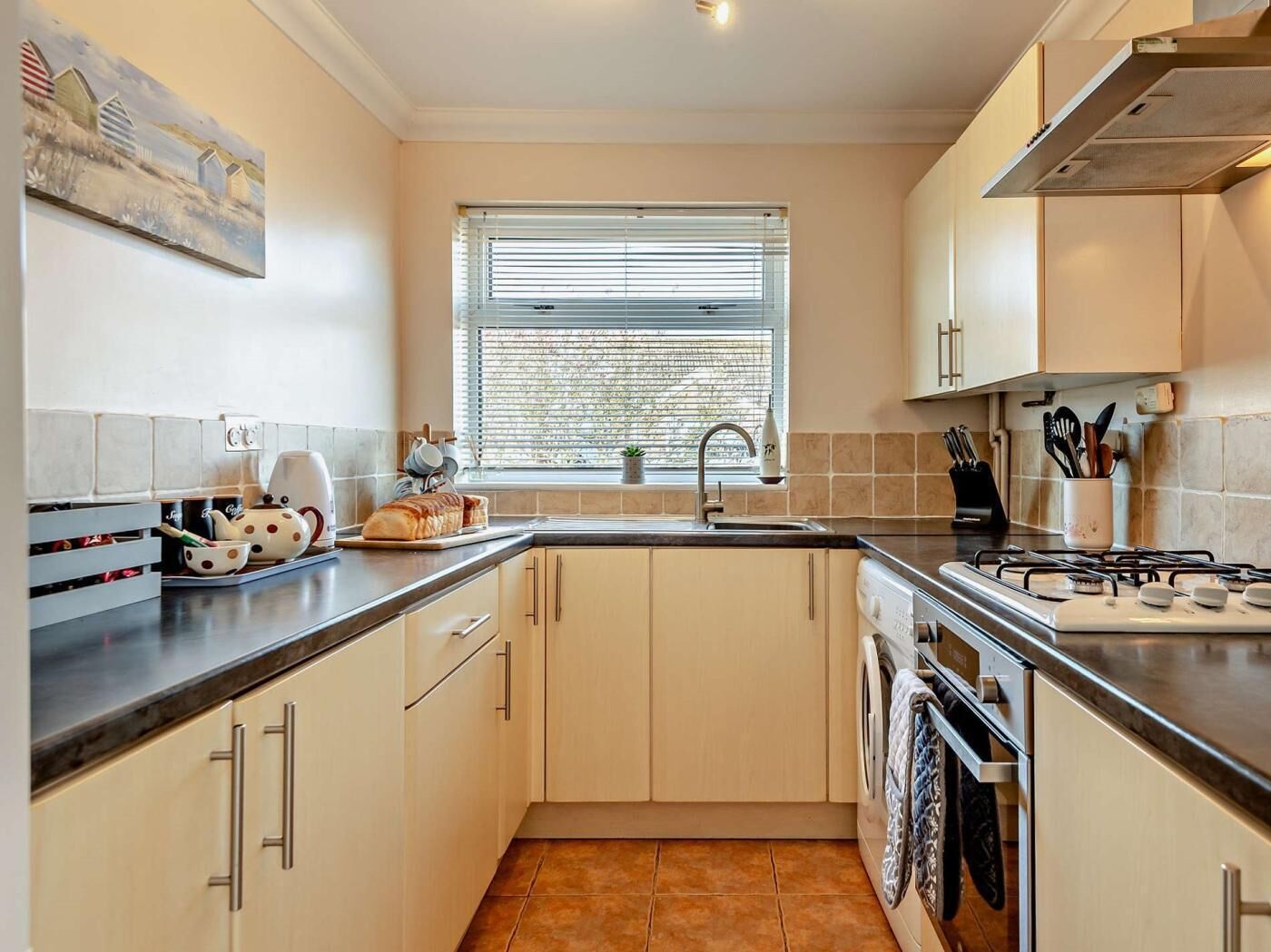 A kitchen with a window, sink, stove, and cabinets.