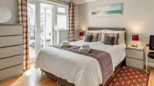 Een slaapkamer met een bed, nachtkastjes, een lamp, een stoel, uitzicht op de omgeving en een schilderij aan de muur.