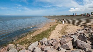 Een kuststrand met een rotsachtige voorgrond, een zandstrand en een helderblauwe lucht.
