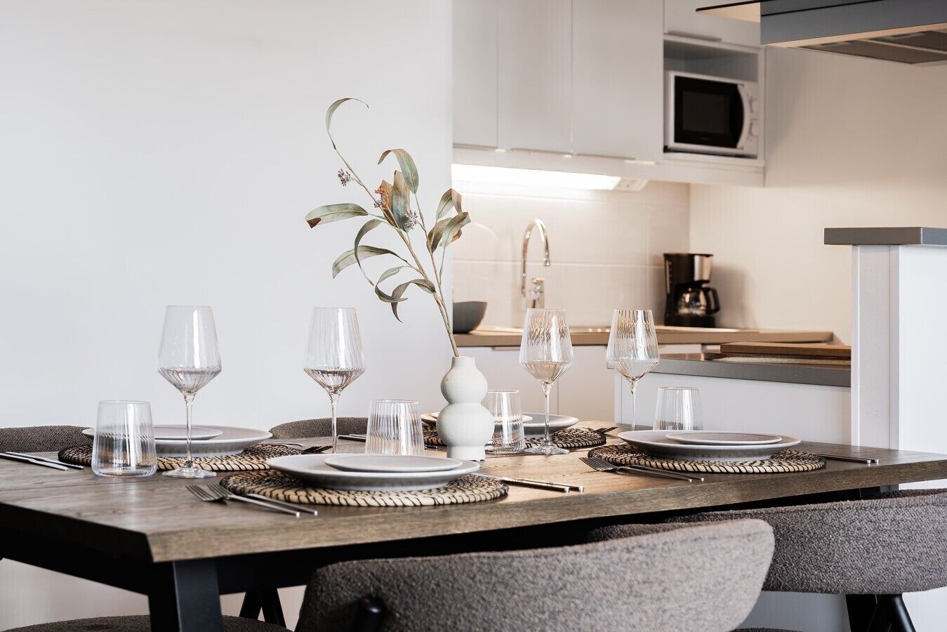 A dining table set with plates, glasses, and a vase with a plant.