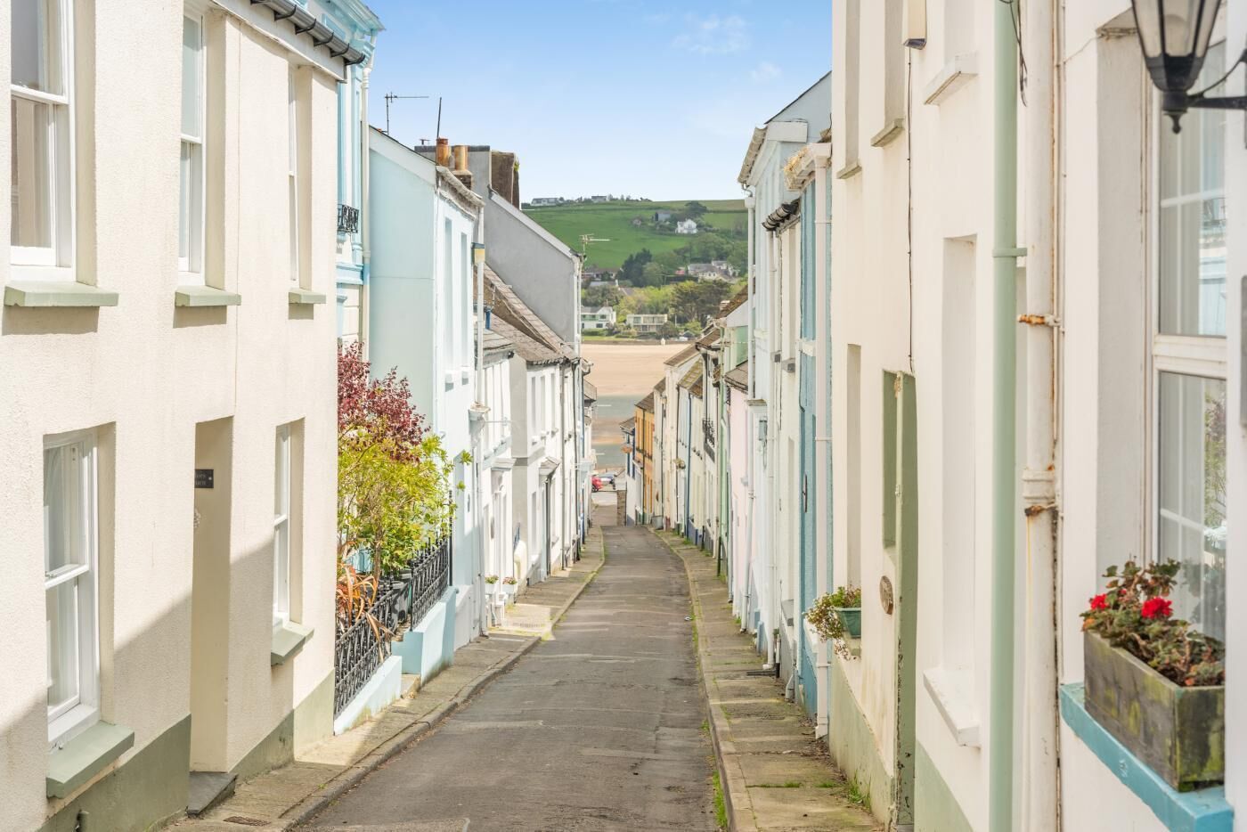 A narrow street lined with traditional buildings, a clear sky, and a distant view of a beach.