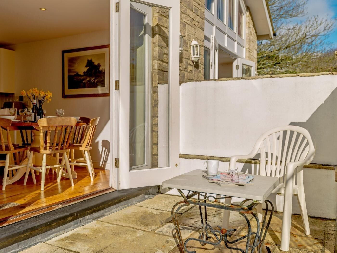 An open patio with a dining table and chairs, a white chair, and a table with a magazine.