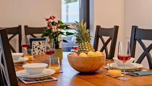 Una mesa de comedor con un bol de frutas de madera, copas de vino y platos.