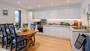 Una cocina moderna con armarios blancos, una mesa de comedor de madera y una pequeña isla con pileta.